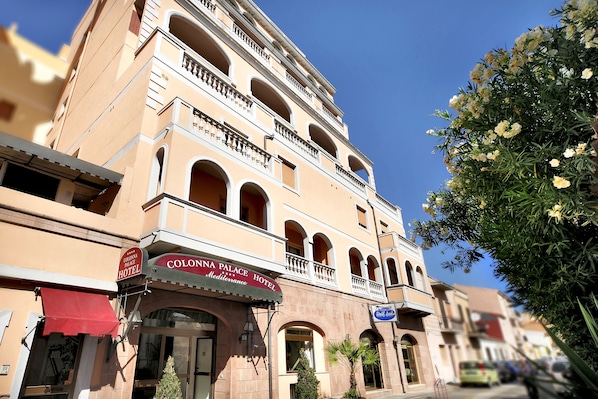 Un hotel con fachada mediterránea, varios balcones y un toldo rojo.