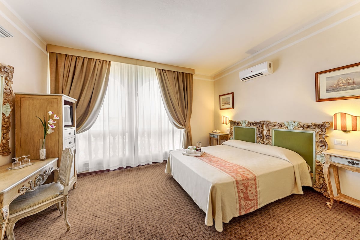 Camera d'albergo con un letto, una scrivania, una sedia, un tavolino e una finestra con tende.