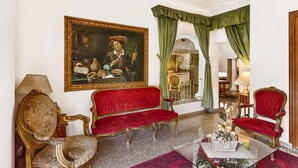 A room with a red velvet sofa, a gold-framed painting, and green curtains.