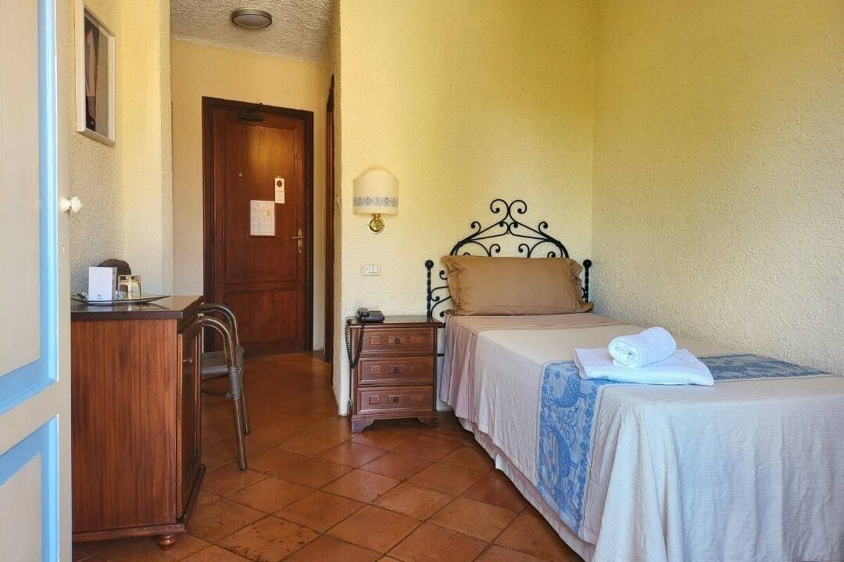 A bedroom with a bed, bedside table, lamp, and a desk with chair.