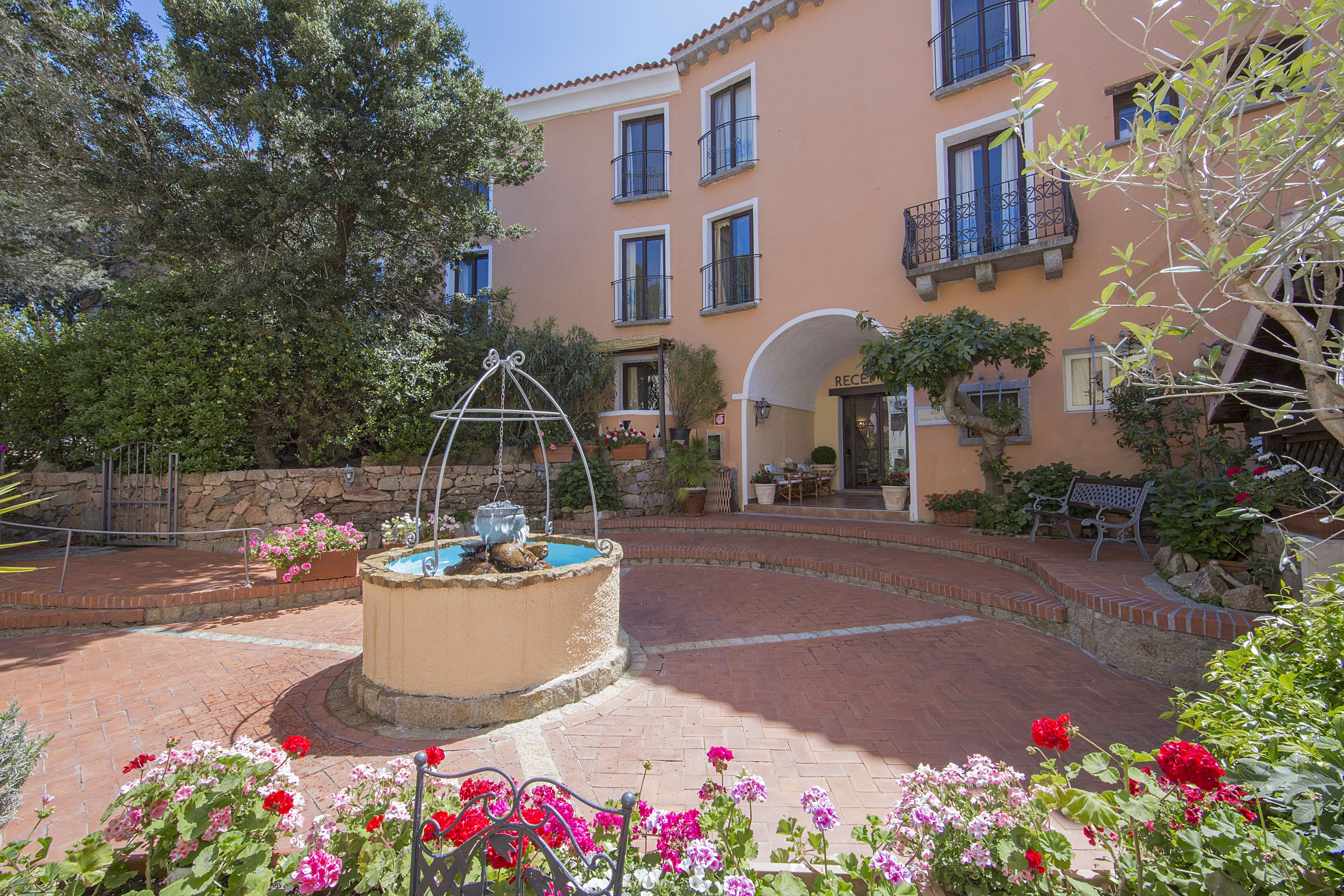 Un patio con una fuente, parterres de flores y un edificio con balcones y ventanas.