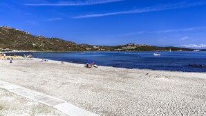 A beach with a clear blue sky, a boat in the water, and a hilly landscape in the background. - Hotel Colonna San Marco (Olbia)