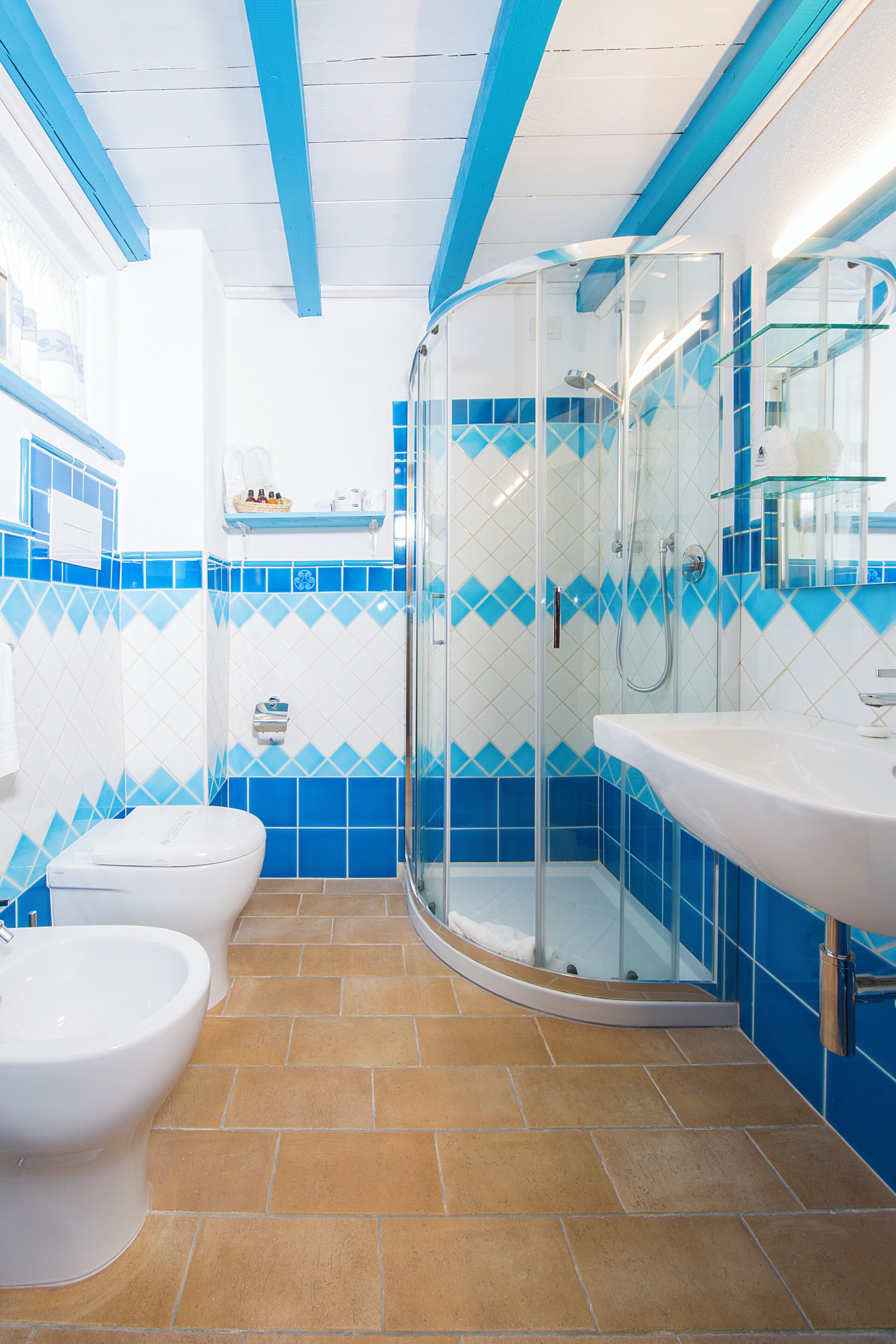 A bathroom with a shower, toilet, and sink, featuring blue and white tiles and a curved glass shower enclosure.