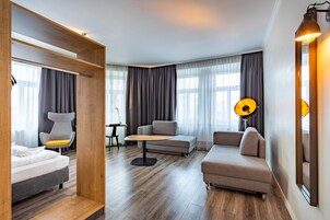 Una habitación de hotel moderna con una cama, dos sofás, una mesita y una lámpara.