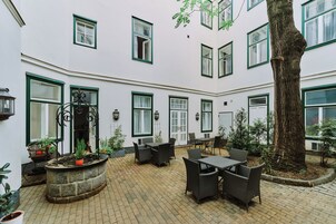 Un patio con mobiliario exterior, una jardinera central con plantas y un árbol grande.