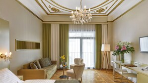 A hotel room with a bed, a sofa, a desk, a chair, a lamp, a vase with flowers, and a large window with curtains. - Hotel Wandl (Vienna)