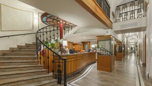 A grand lobby with a curved staircase, a reception desk, and a chandelier. - Hotel Wandl (Vienna)