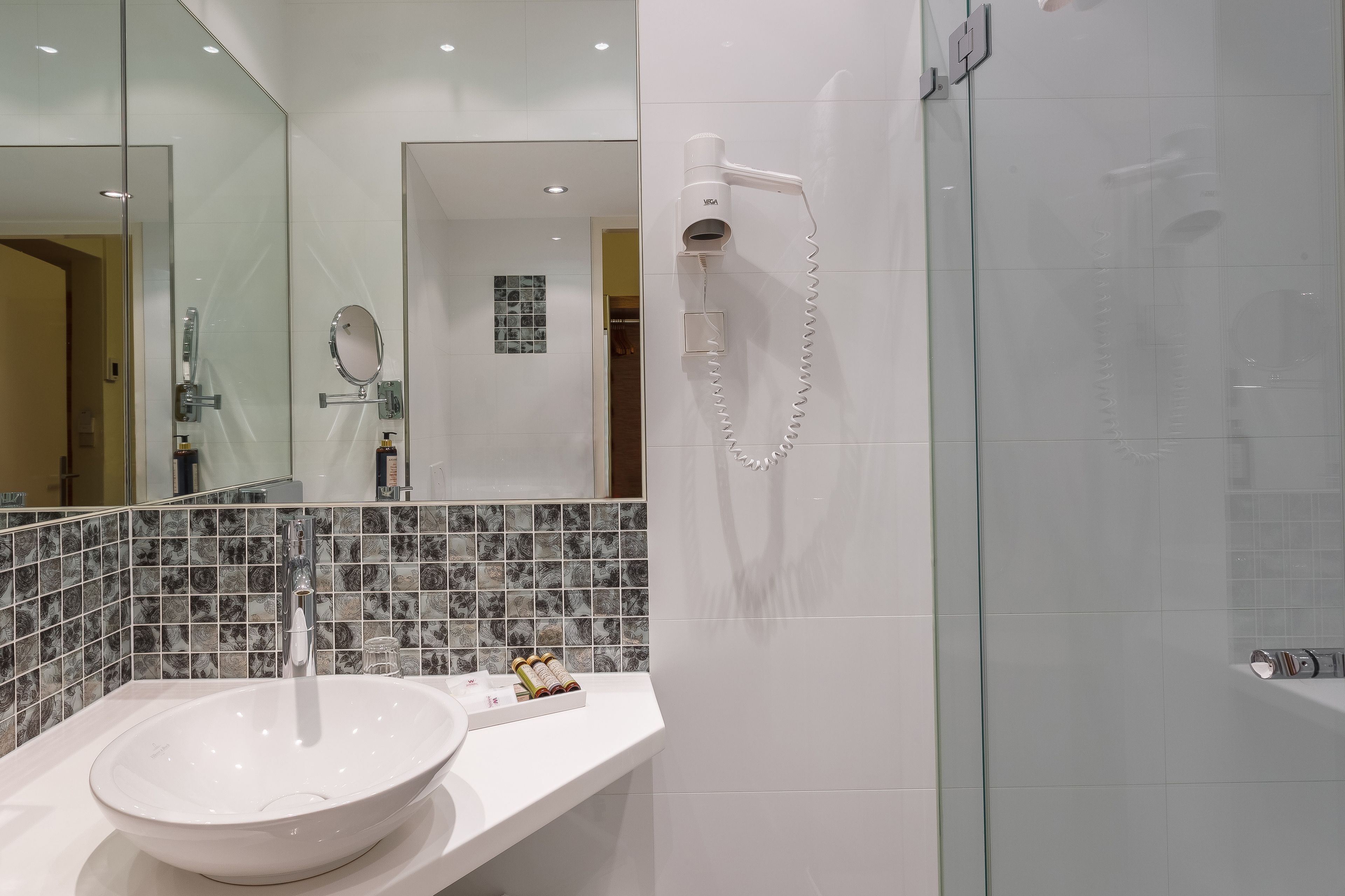 Un baño moderno con lavamanos blanco, secador de pelo de mano y cabina de ducha de vidrio.