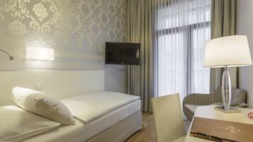 Quarto de hotel com uma cama, uma mesa com luminária, uma televisão e uma janela com cortinas.