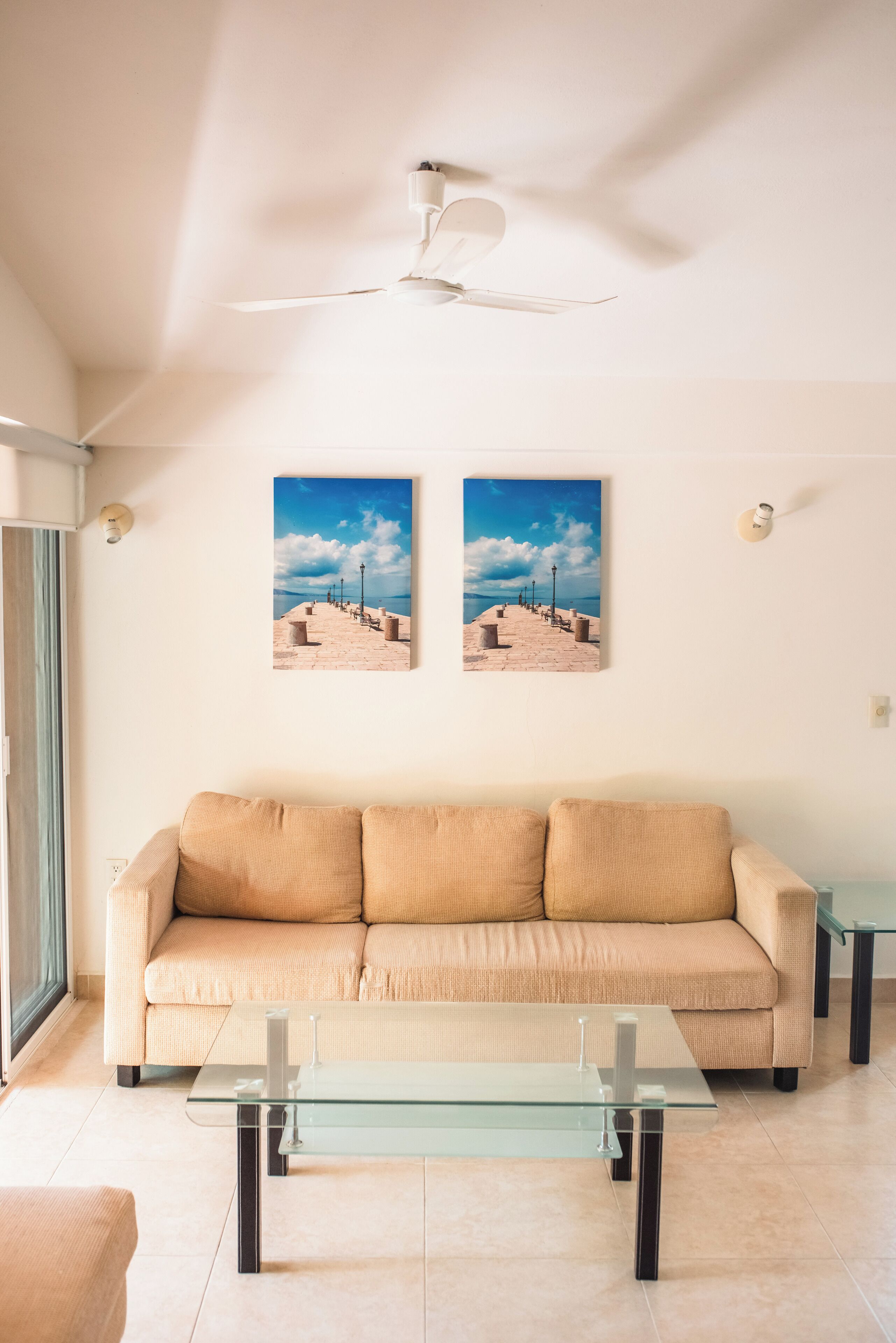 Ein Wohnzimmer mit einem beigefarbenen Sofa, einem Glastisch und zwei gerahmten Bildern an der Wand.