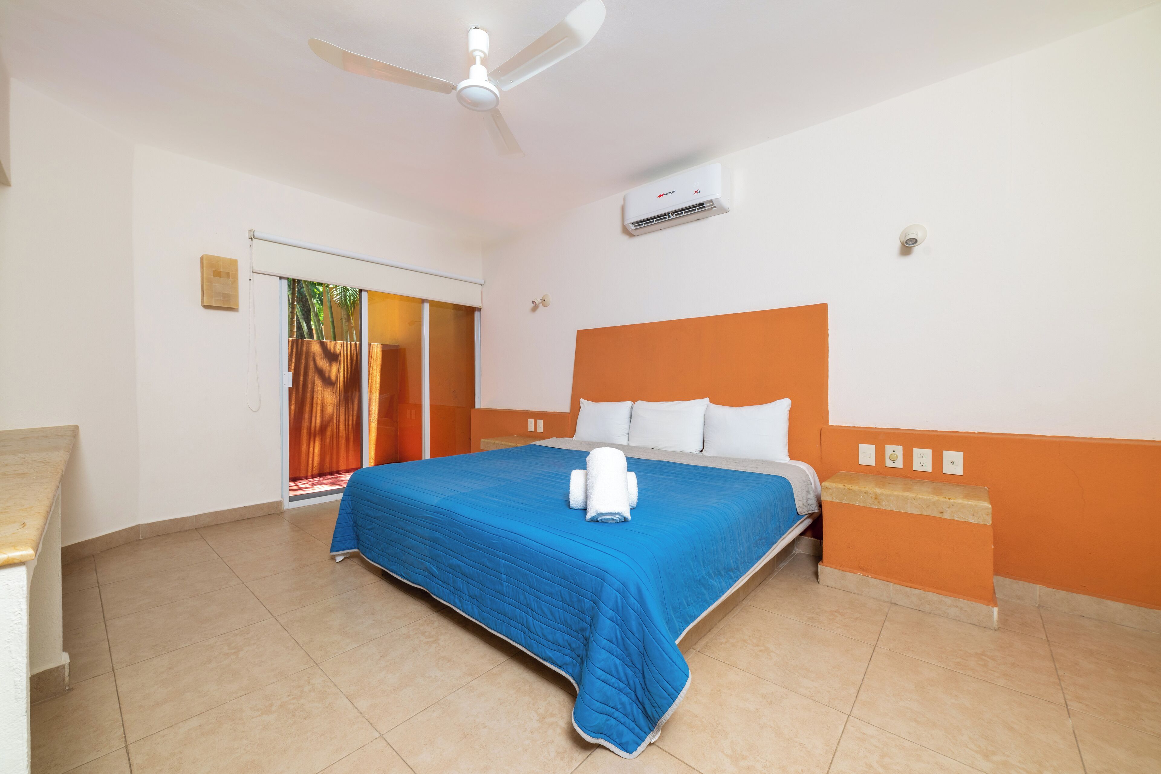 Une chambre d’hôtel équipée d’un lit, d’un ventilateur de plafond, d’un appareil de climatisation et d’une fenêtre avec des rideaux.