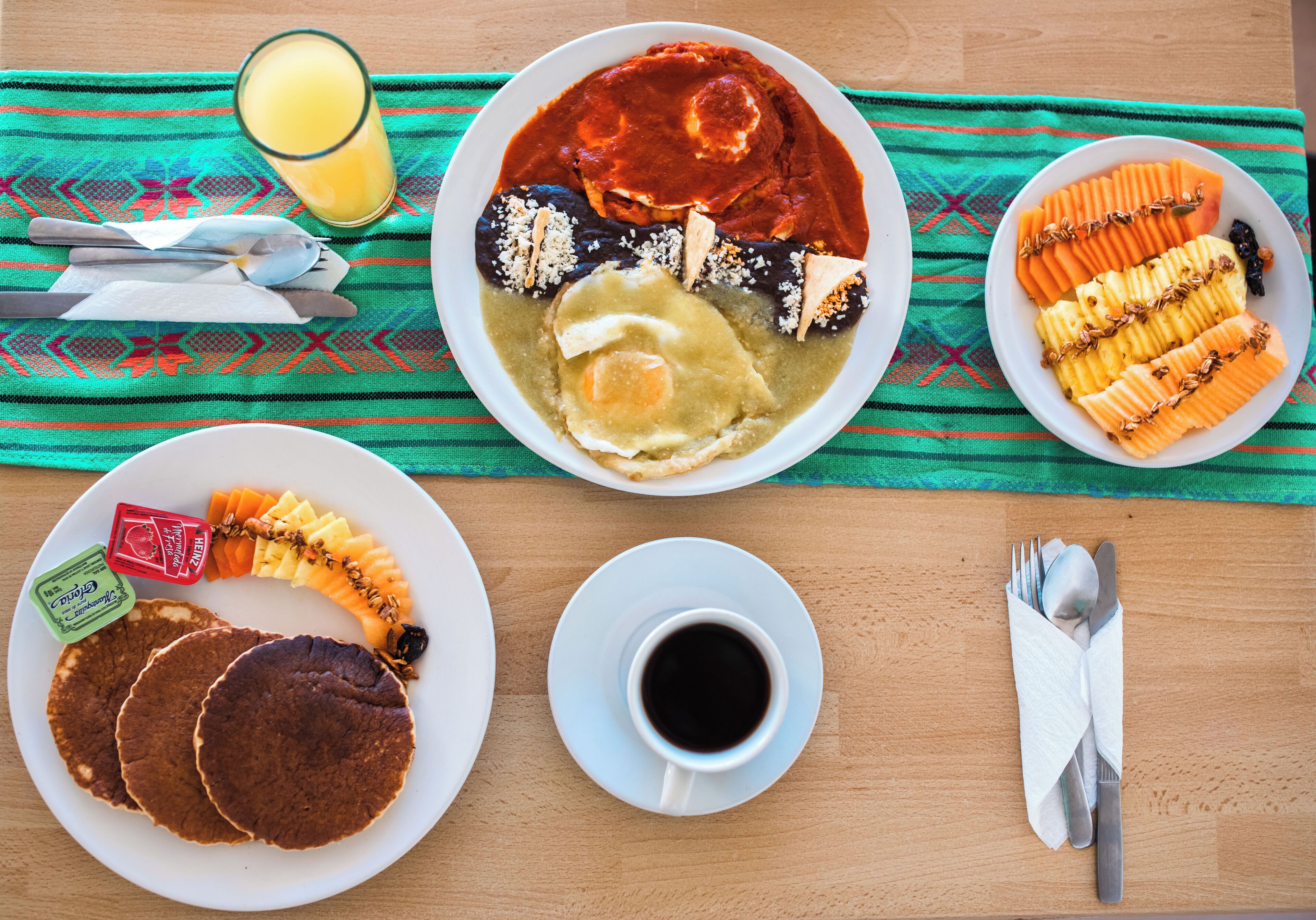 Un desayuno con platos de comida, un vaso de zumo de naranja y una taza de café sobre una mesa de madera.