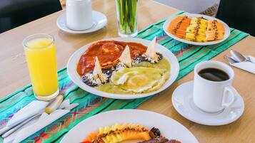 A table with breakfast items including pancakes, a plate of fruit, a cup of coffee, and a glass of orange juice.