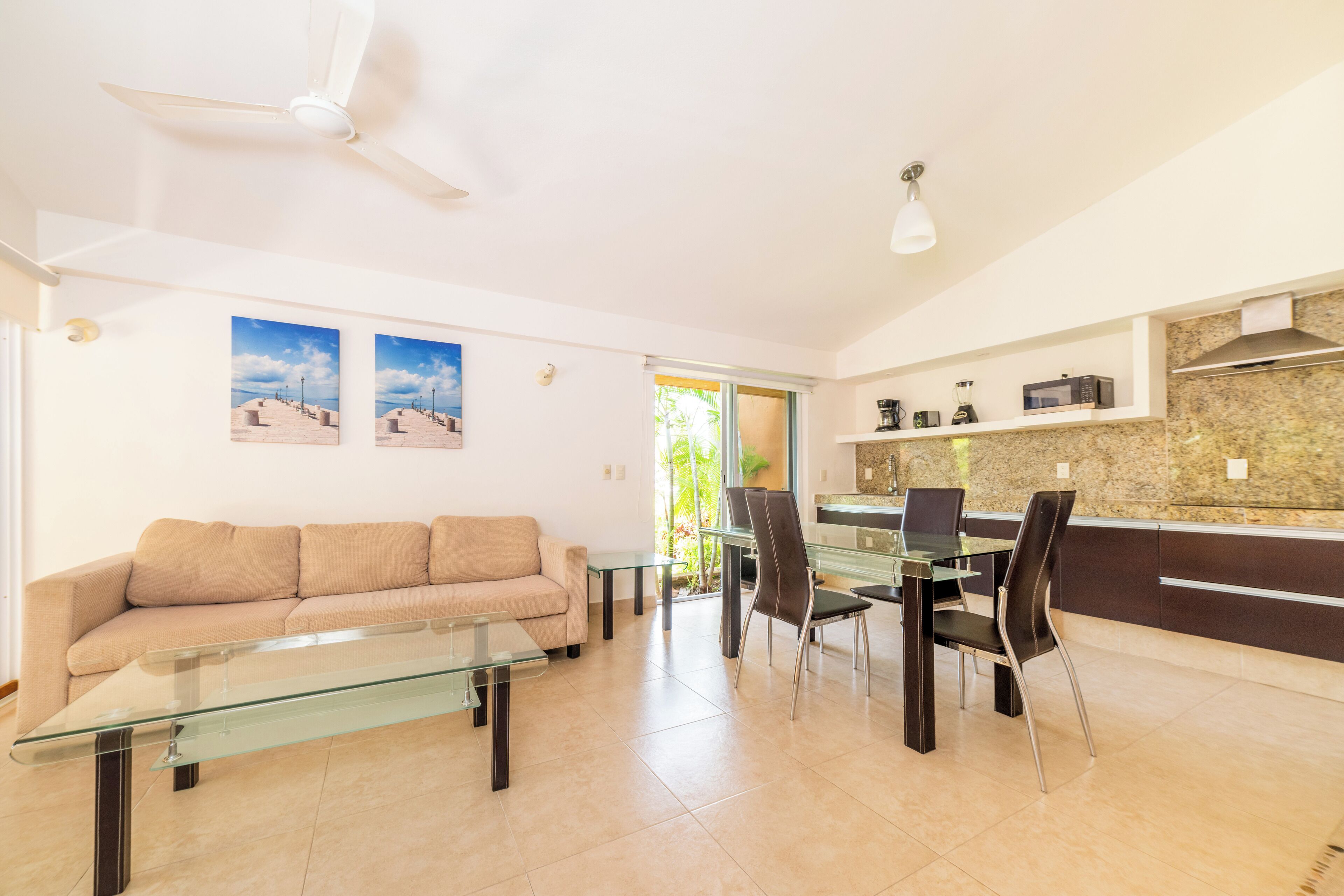 A modern living room with a glass coffee table, a beige sofa, and a dining area with a glass table and chairs.