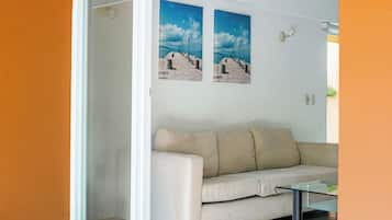 Una habitación con puerta de cristal corredera que da a un balcón, un sofá color beige y dos cuadros en la pared.