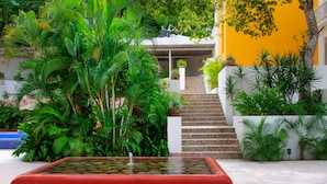 A tranquil indoor garden with a water feature, lush greenery, and a staircase leading to a covered area. - Hotel Ixzi Plus (Ixtapa)