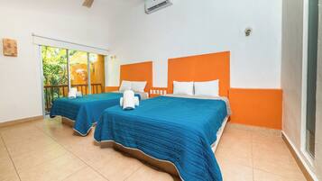 Une chambre d’hôtel avec deux lits, chacun doté d’une tête de lit orange et de draps bleus. On peut voir un ventilateur de plafond et un appareil de climatisation.