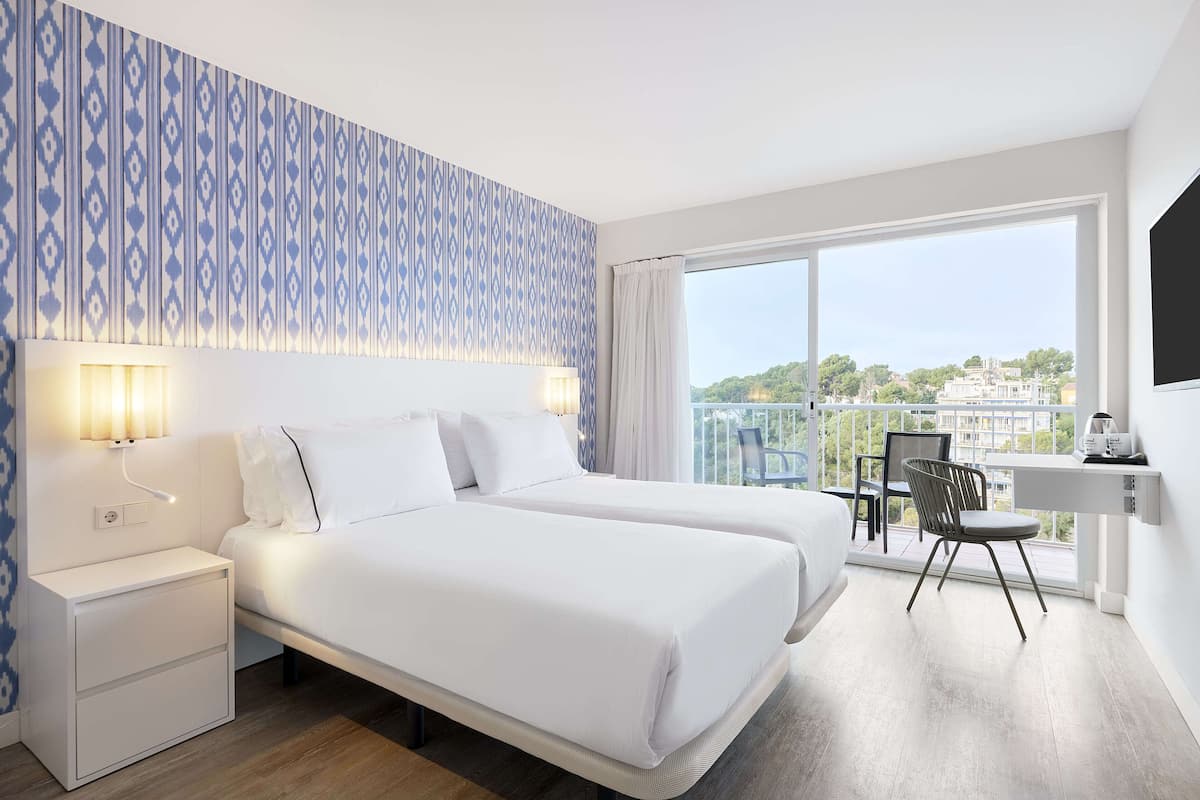 A hotel room with two beds, a desk, and a view of the city.