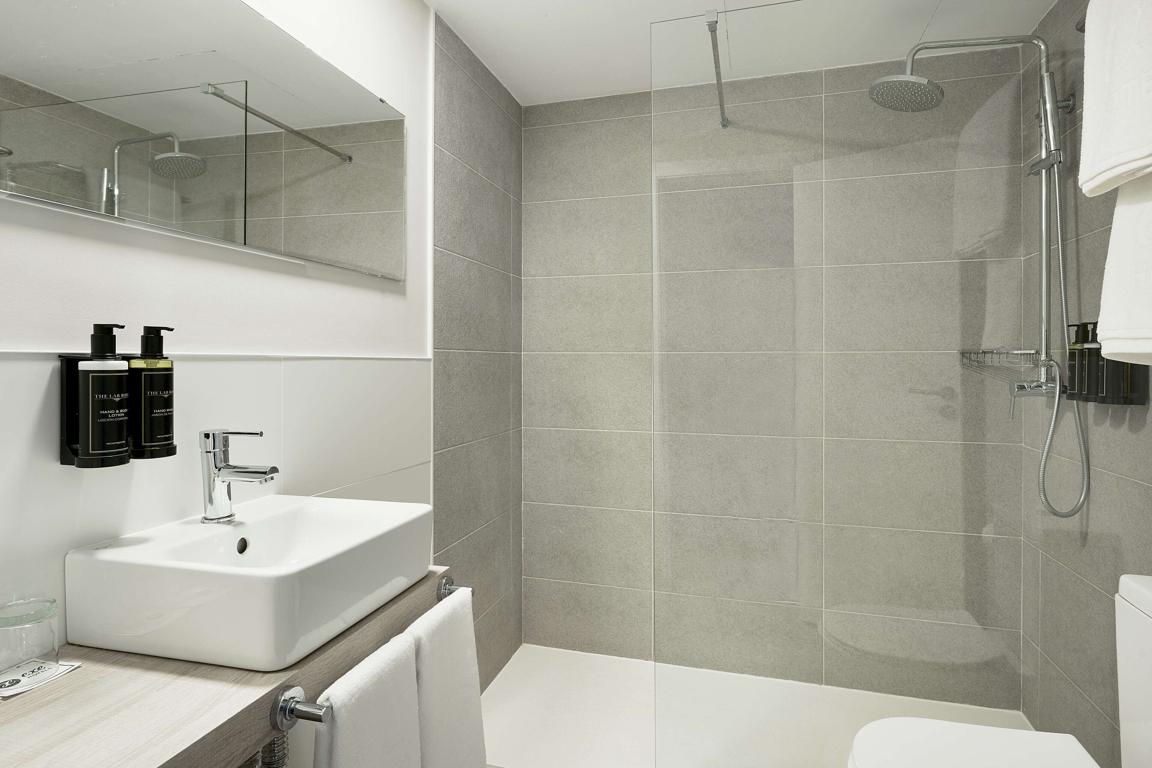 Un baño moderno con un lavamanos blanco, una cabina de ducha con mampara de vidrio y un inodoro.