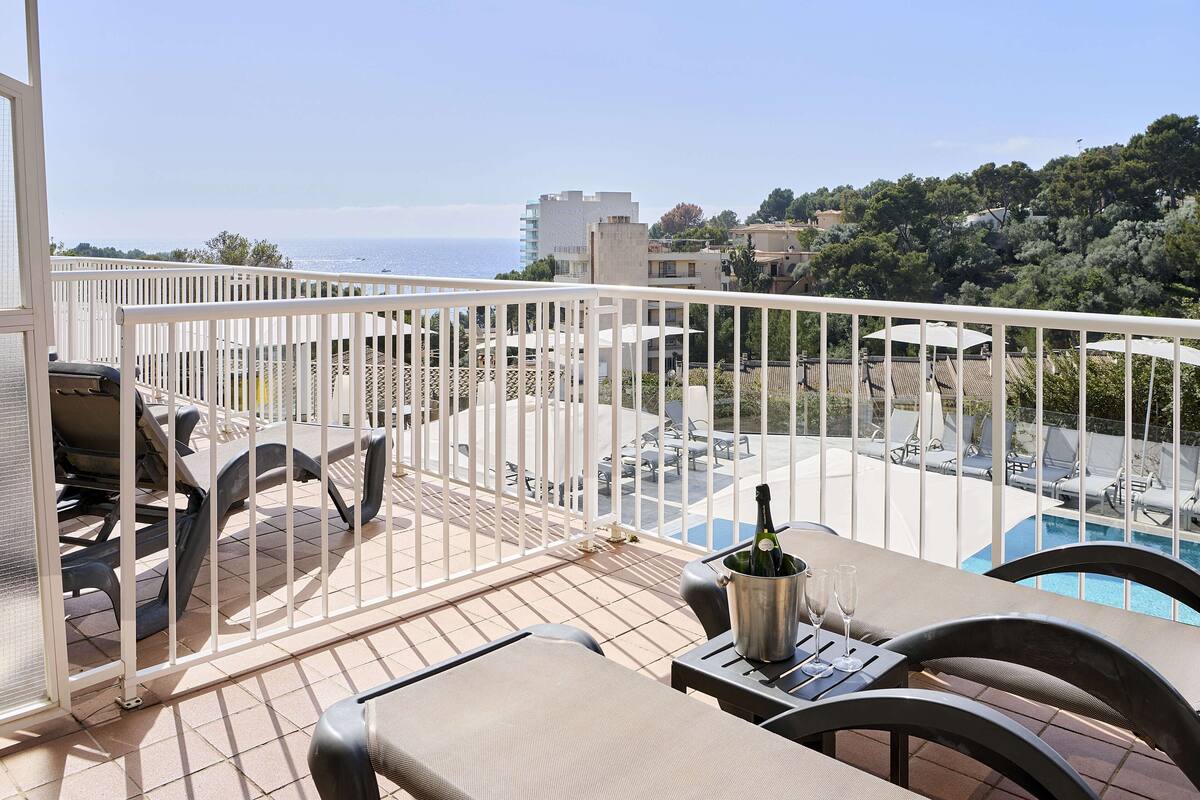 A balcony with a pool view, outdoor seating, and a bottle of champagne.