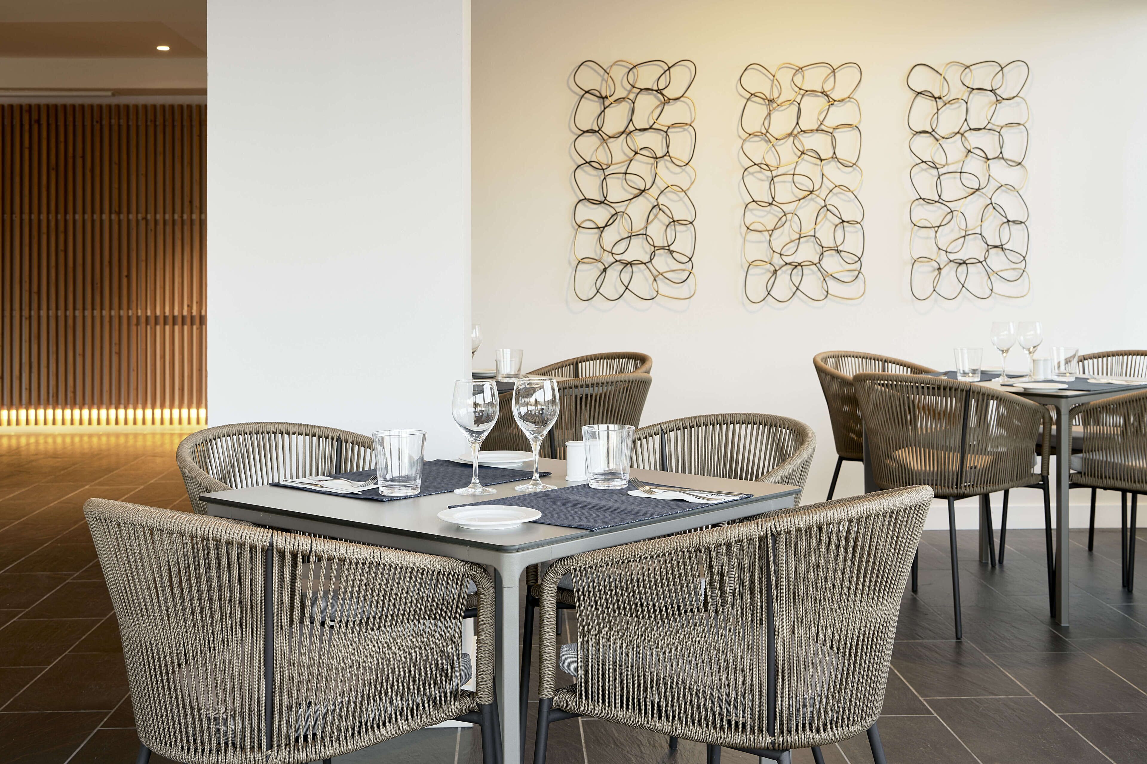 Un comedor moderno con sillas de mimbre y una mesa rectangular dispuesta para una comida.