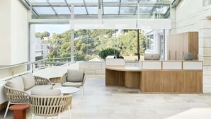 Un área de lounge al aire libre moderna con techo de vidrio, mobiliario de mimbre y mostrador de recepción de madera.