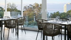 Comedor con sillas de mimbre y una mesa dispuesta para dos, con vistas a un paisaje de árboles y agua.