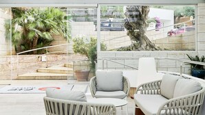 Un área de estar exterior moderna con mobiliario de mimbre, un muro de piedra y vista a un estacionamiento con escaleras.