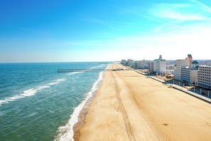 Una playa con un muelle que se adentra en el océano, junto a una hilera de hoteles con balcones con vista al mar.