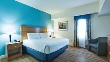 A hotel room with a large bed, wooden nightstands, a desk, a chair, and a painting on the wall.