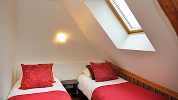 Een kamer met twee bedden, elk voorzien van rode beddengoed en kussens met bloemenprint, een klein nachtkastje en een dakraam erboven.