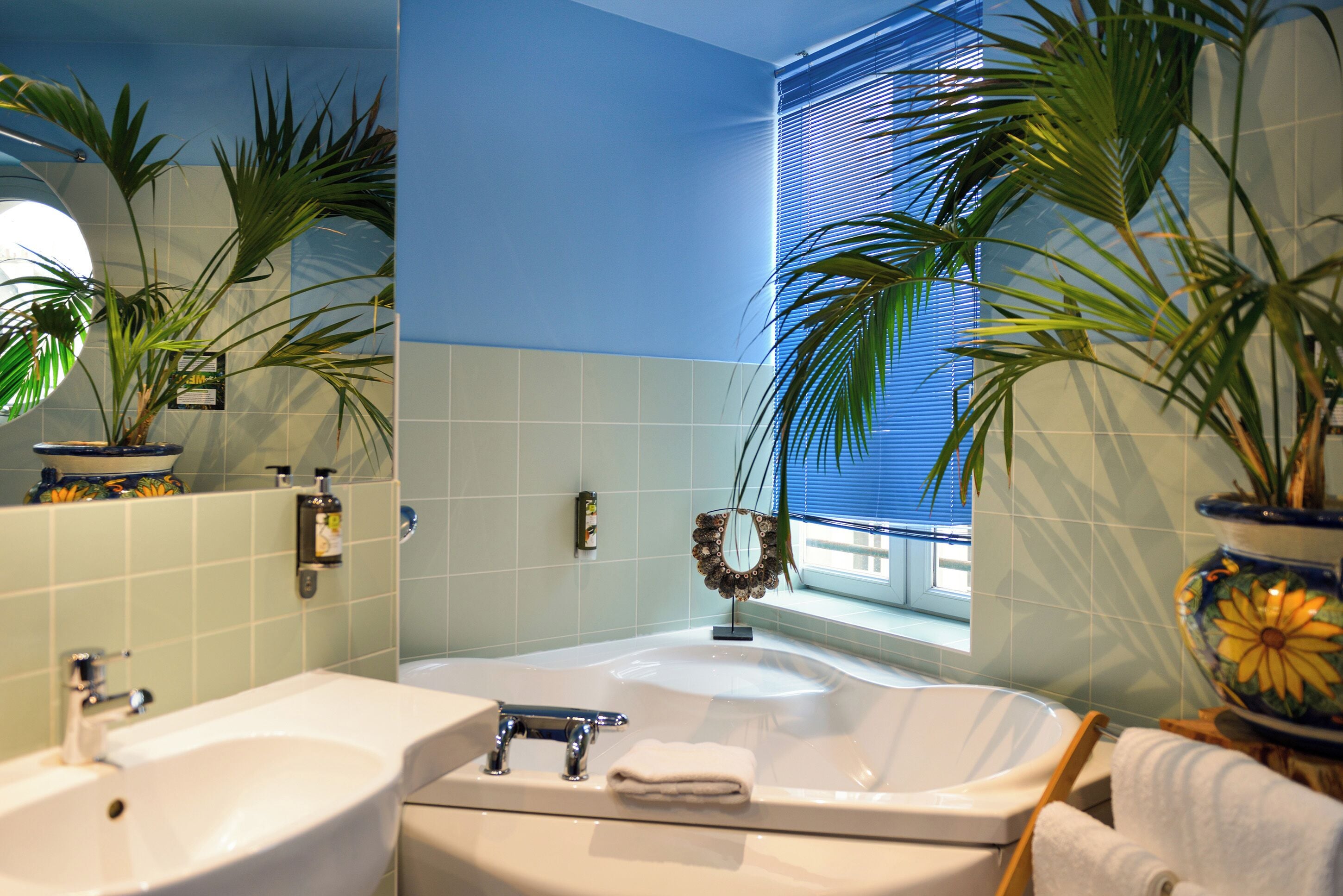 Une salle de bain avec une baignoire, un lavabo et deux plantes en pot.