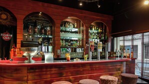 A bar area with a red counter, shelves with bottles, and three animal-patterned stools. - Logis Hôtel le St Georges Vendôme (Vendome)