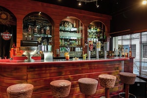 Una zona de bar con mostrador rojo, estantes llenos de botellas y tres taburetes con estampado de animales.