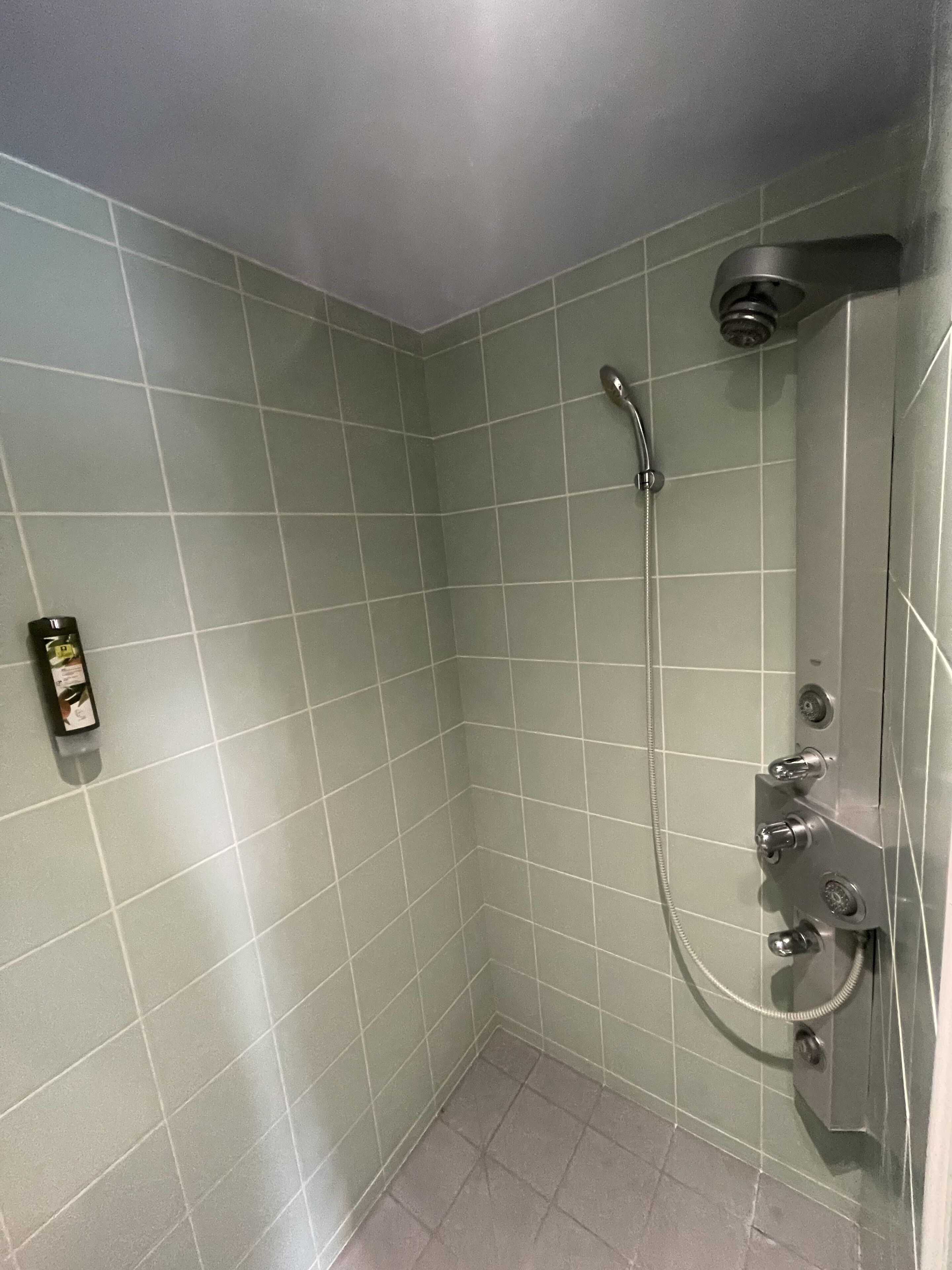 Un baño pequeño con azulejos, una ducha de mano y un grifo instalado en la pared.