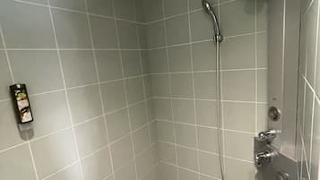 Une petite salle de douche carrelée, dotée d’un pommeau de douche à main et d’un robinet fixé au mur.