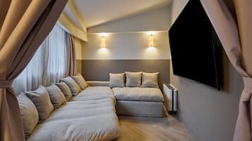 A modern bedroom with a sectional sofa, a flat-screen TV, and wall-mounted lighting.