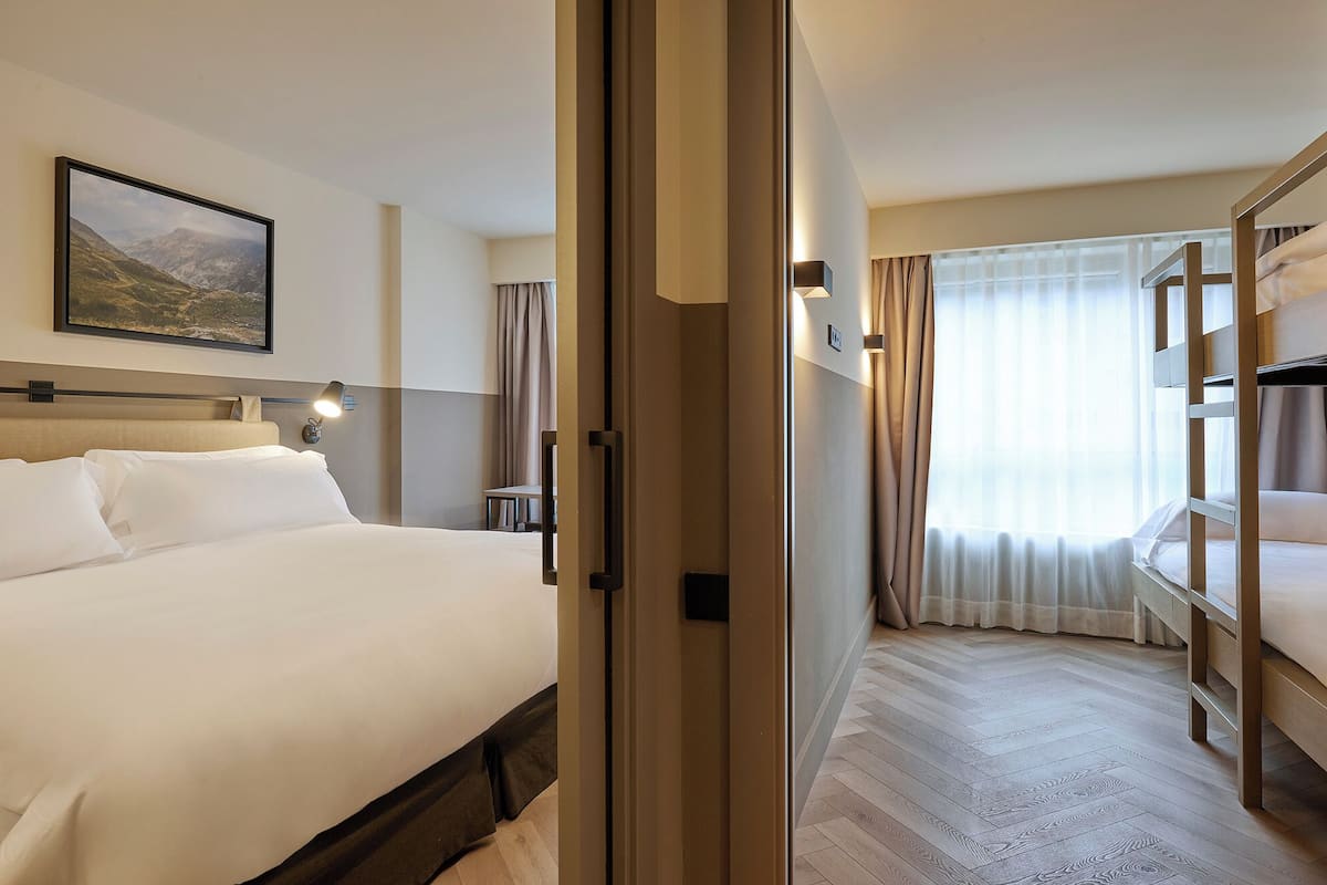 Habitación de hotel con cama, escritorio, silla, ventana con cortinas y literas.