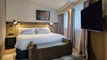 A hotel room with a large bed, a flat-screen TV, a bedside table with a lamp, and a painting on the wall.