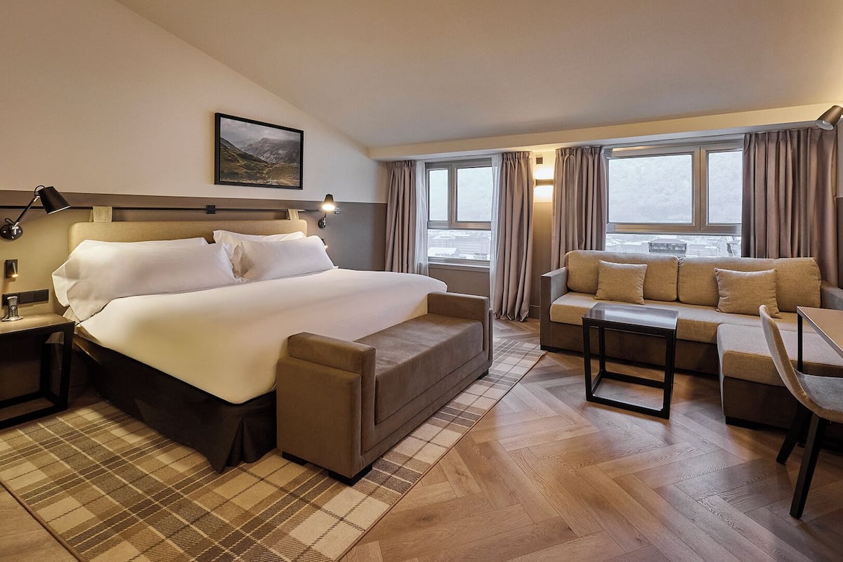Habitación de hotel con una cama grande, un sofá, un escritorio y una ventana con cortinas.