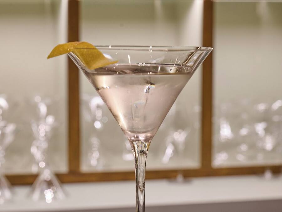 A martini glass with a lemon twist on a reflective surface.