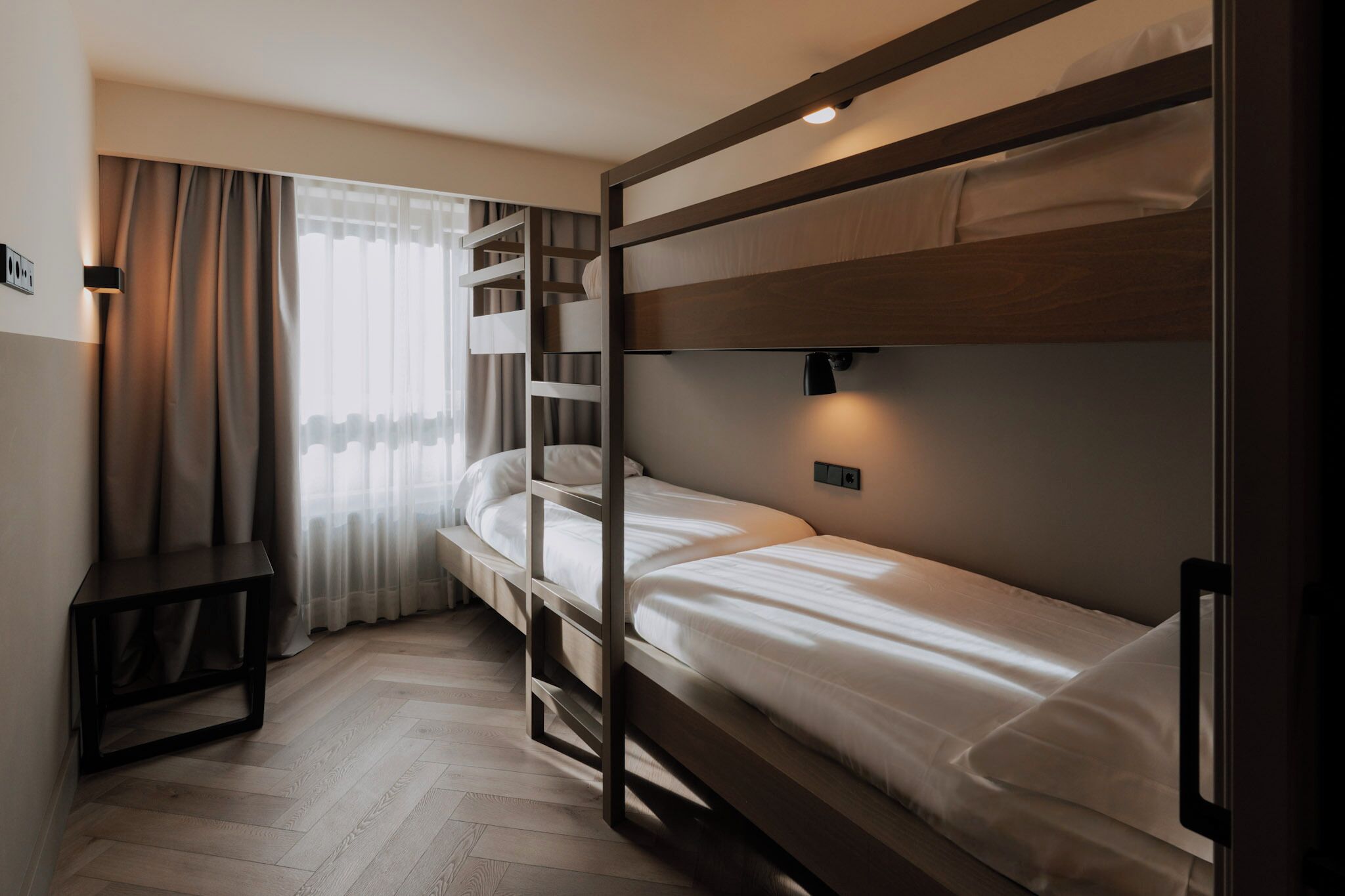 Habitación con literas, un escritorio, una ventana con cortinas y una lámpara de pared.