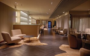 A hotel lobby with a bar, seating area, and a view of the city.