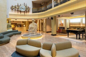 A spacious lobby with a grand piano, a unique sculpture centerpiece, and a modern chandelier.