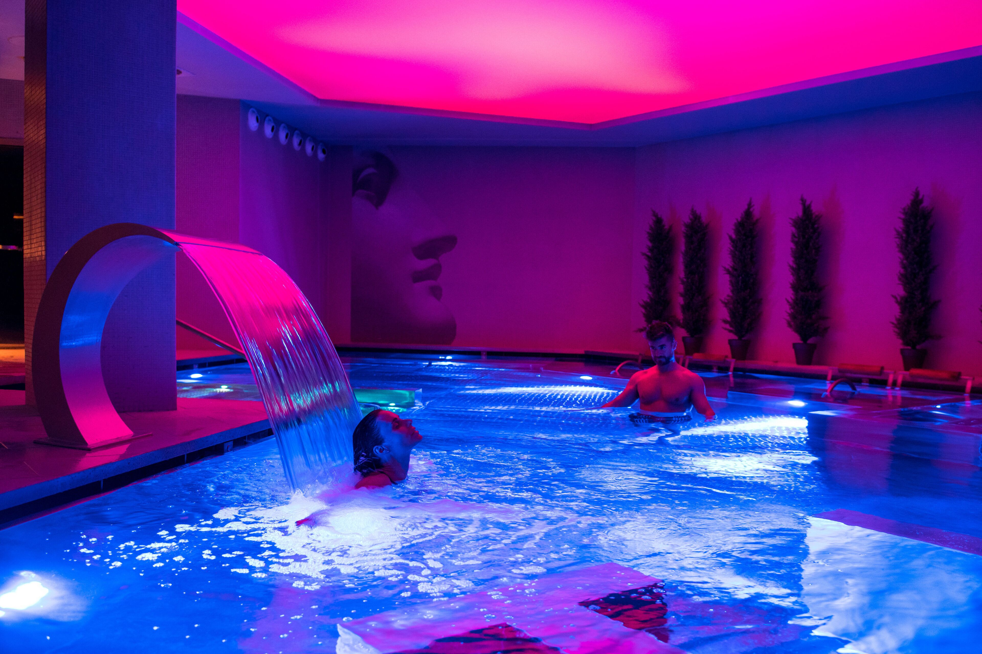 Una piscina con fuente de agua y una persona nadando.
