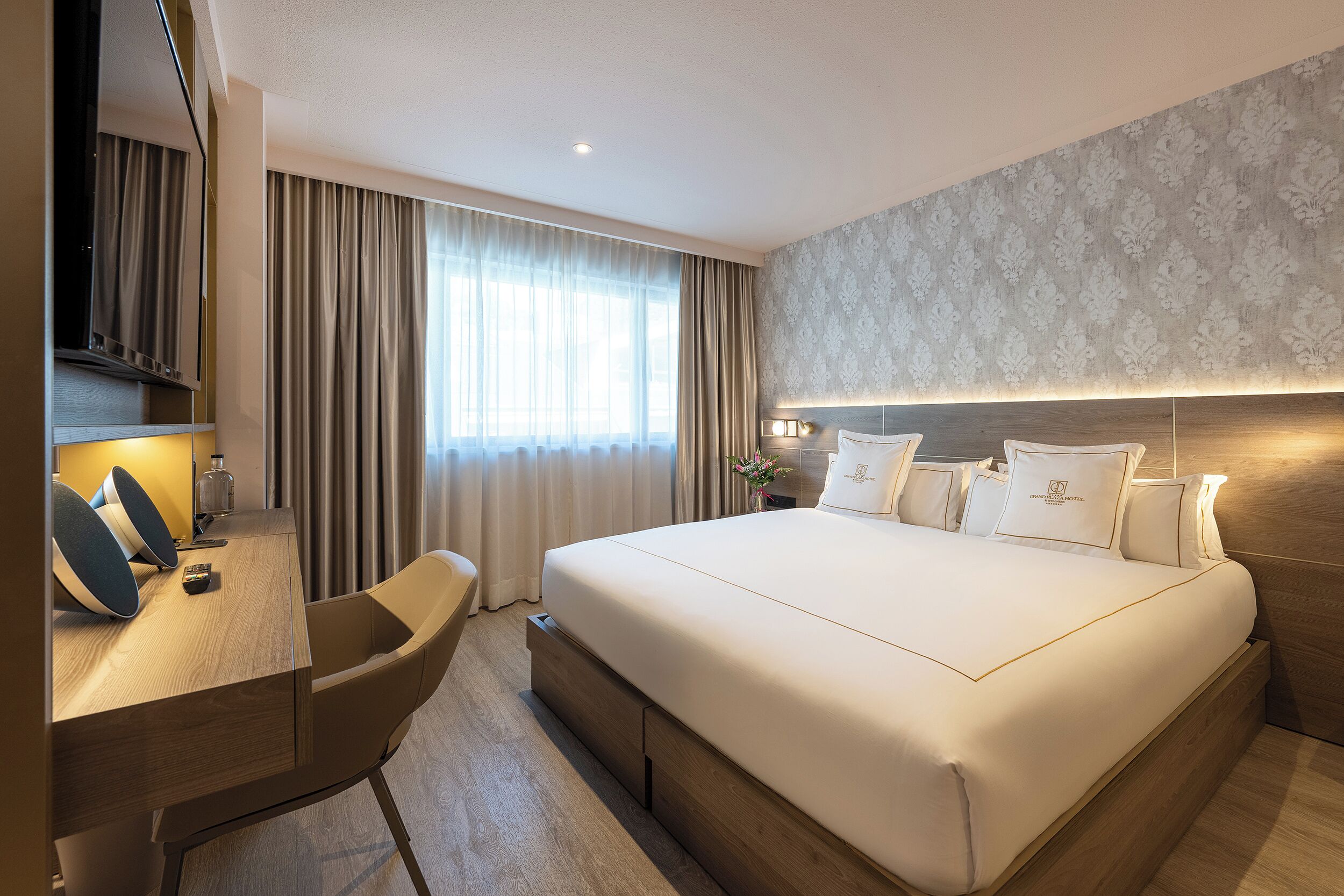 Habitación de hotel con una cama grande, un escritorio con silla, un espejo y una ventana con cortinas.