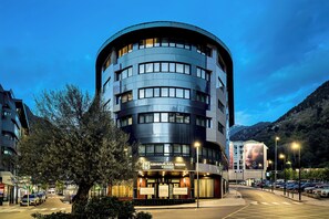 A modern hotel with a curved facade, multiple floors, and a sign indicating amenities like a spa and conference rooms. -  Grand Plaza Hotel & Wellness (Andorra la Vella)