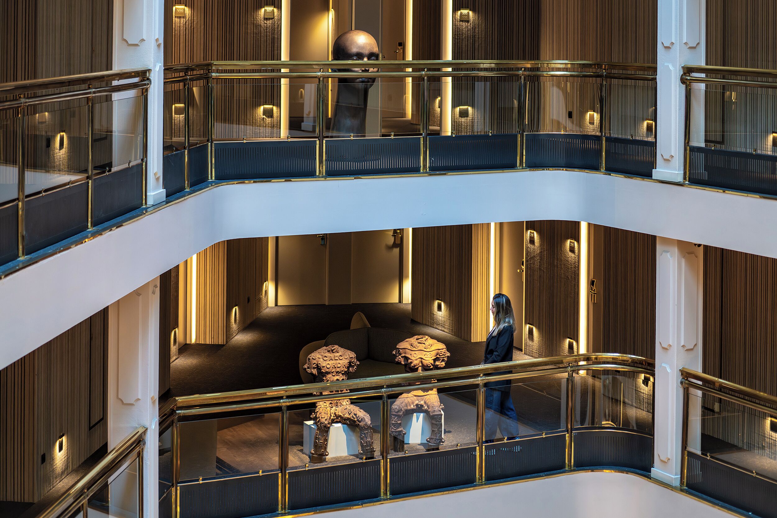A multi-level interior with glass railings, a central seating area with cushions, and a person walking.