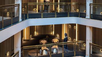 A multi-level interior with glass railings, a central seating area with cushions, and a person walking.