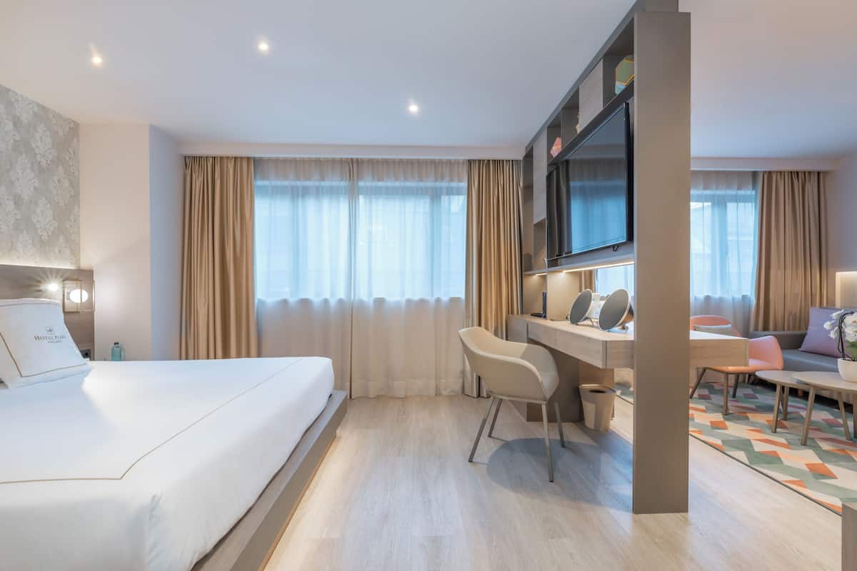 A modern hotel room with a large bed, a desk with a chair, a flat-screen TV, and a sofa.